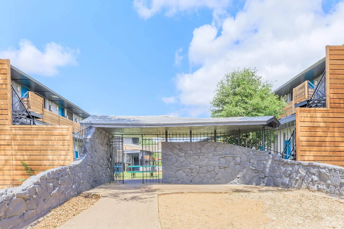 Stone wall with a metal gate under a covered walkway connecting two buildings, with picnic tables visible beyond at 3311 at Vernon in Dallas