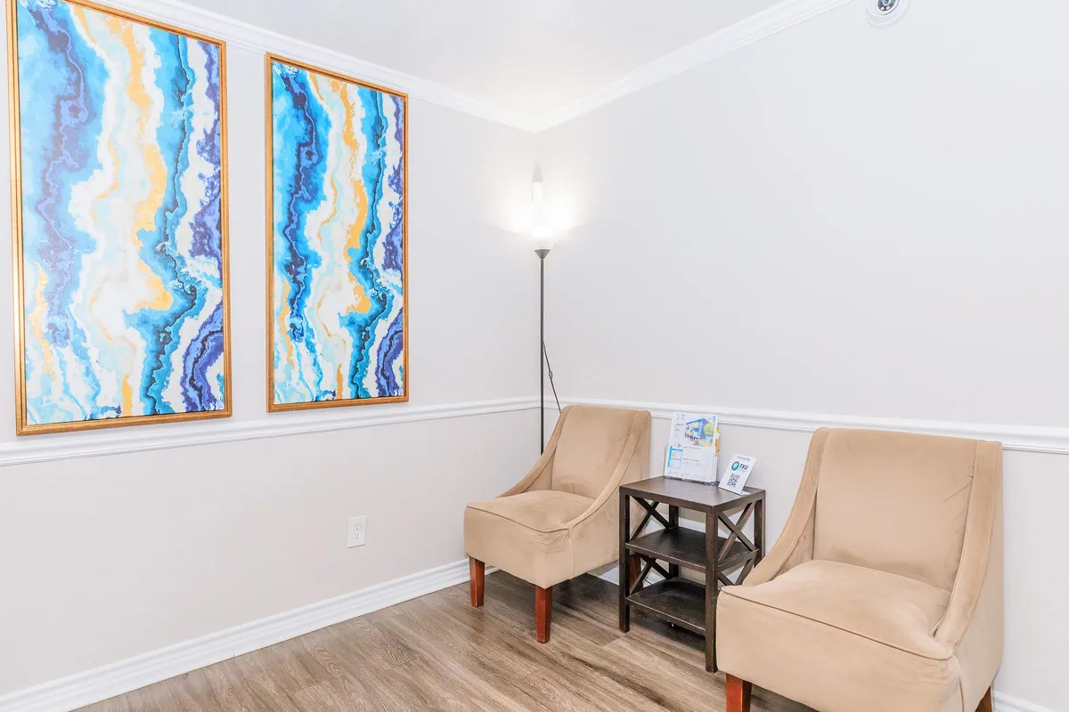 Leasing office seating area with two upholstered chairs, a side table, a floor lamp, and framed abstract wall art at 3311 at Vernon in Dallas