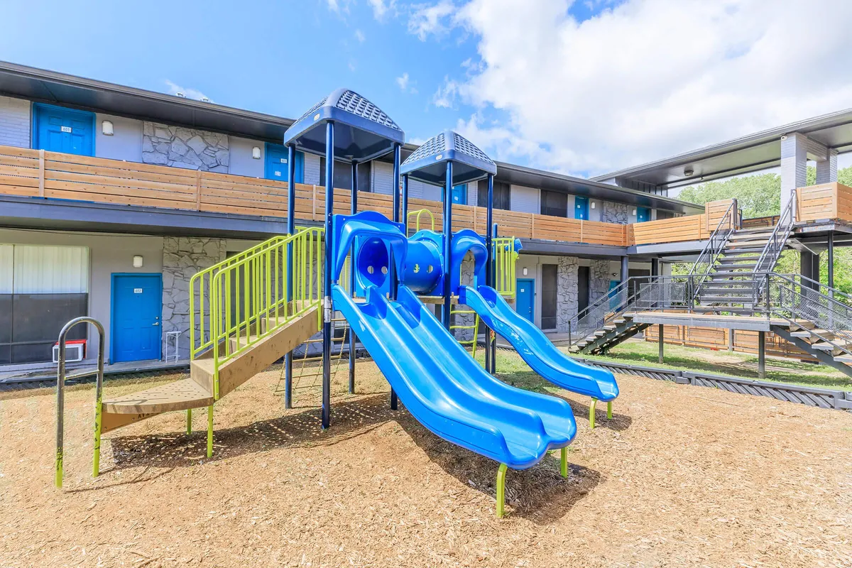Playground with blue slides, a crawl tunnel, and canopy towers on mulch beside a two-story building at 3311 at Vernon in Dallas