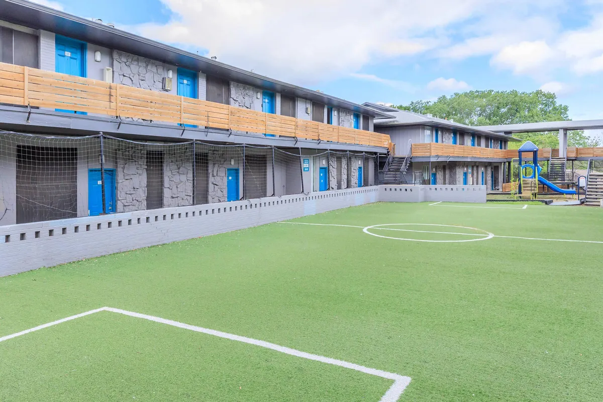 Turf soccer field with white line markings and netting beside two-story buildings, with a playground in the background at 3311 at Vernon in Dallas