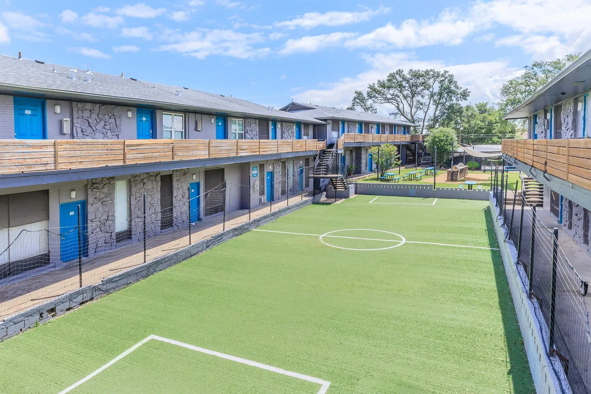 Elevated view of a turf soccer field with netting along building walkways and a picnic area in the distance at 3311 at Vernon in Dallas