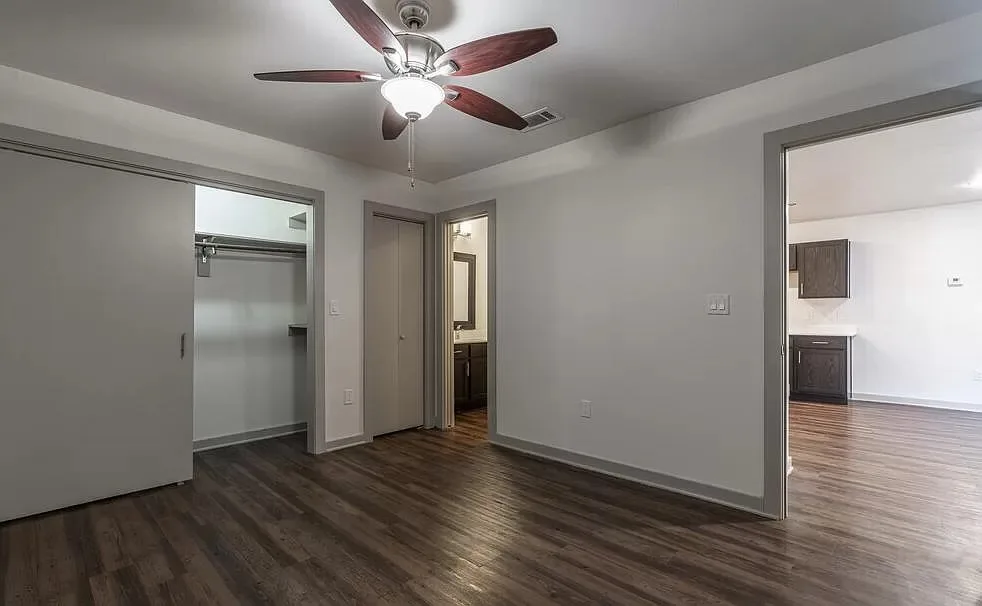 Bedroom with a ceiling fan and an open walk-in closet, an en-suite bath doorway, and a view toward the kitchen