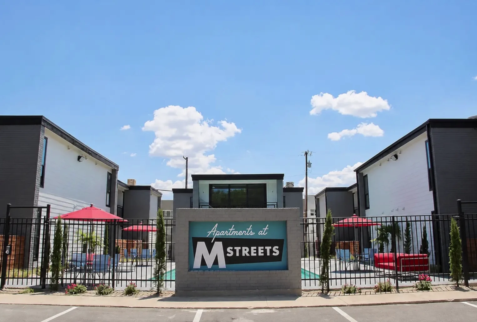 Retro 'Apartments at M streets' monument sign flanked by the pool courtyard and modern black-and-white buildings