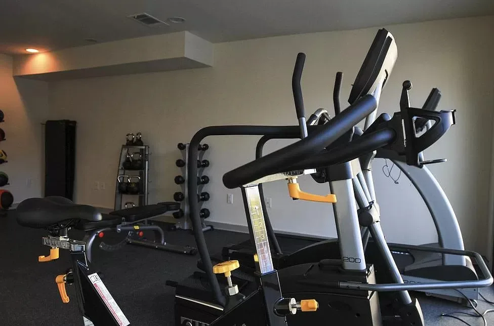 Fitness center with an elliptical machine, upright bike, weight bench, and free-weight rack on rubber flooring