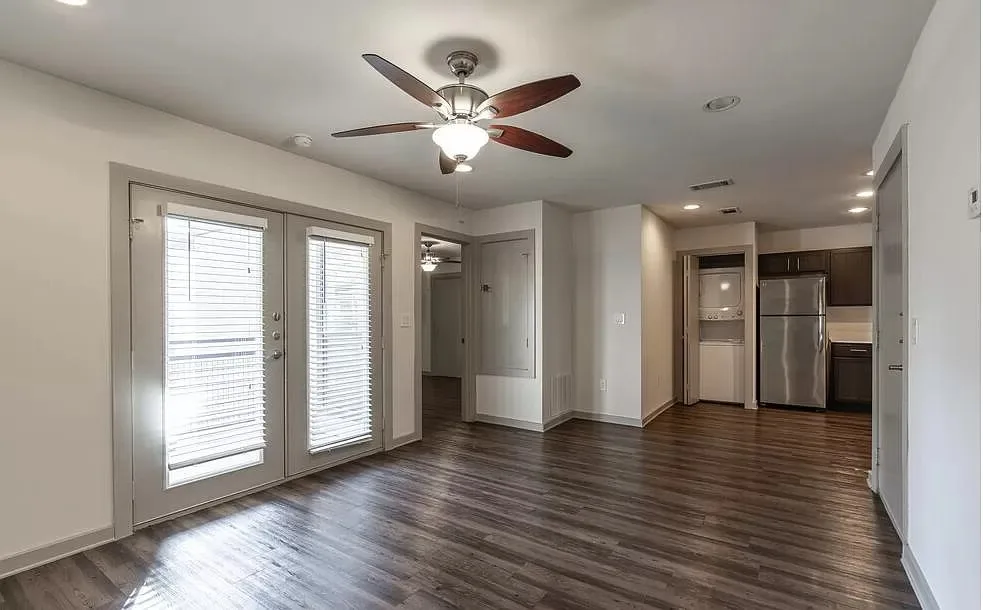 Living area with a ceiling fan and French patio doors beside a kitchen with a stacked laundry alcove
