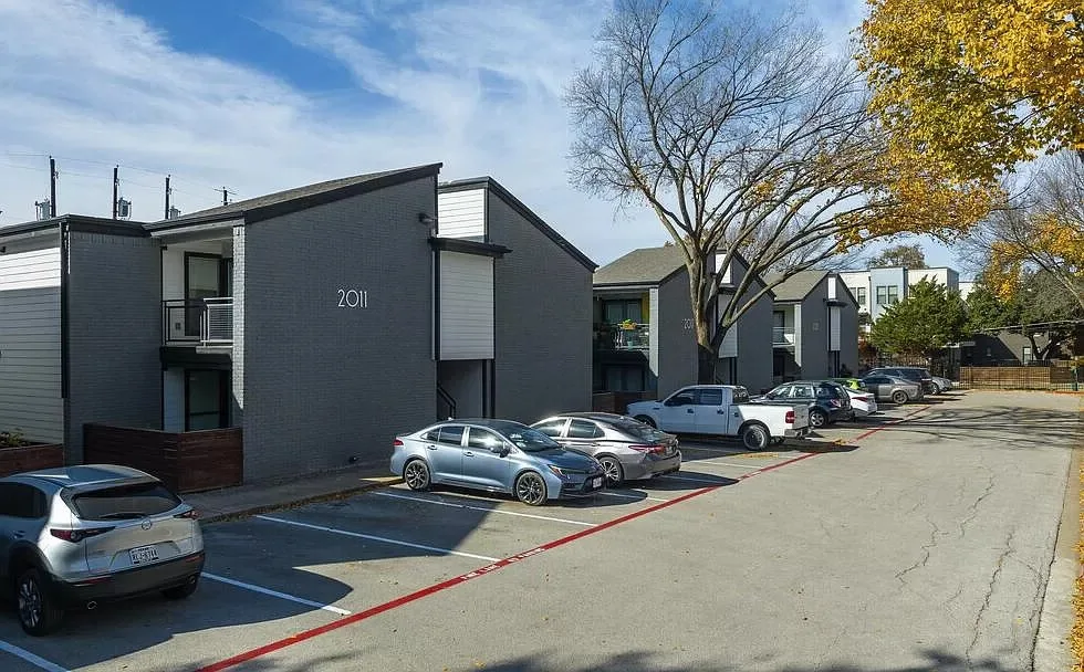 Surface resident parking lot alongside the dark-brick building shaded by mature trees