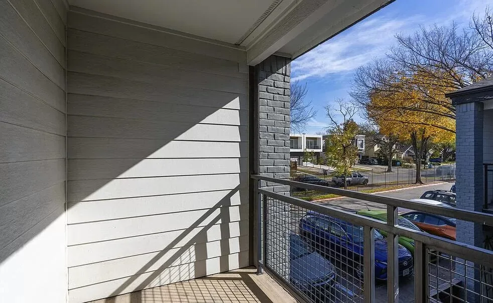 Covered private balcony with a metal railing overlooking the parking lot and neighboring townhomes