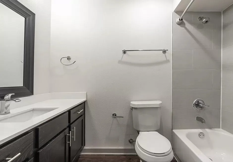 Bathroom with a dark-wood vanity, quartz top, framed mirror, and a tiled tub-and-shower combination