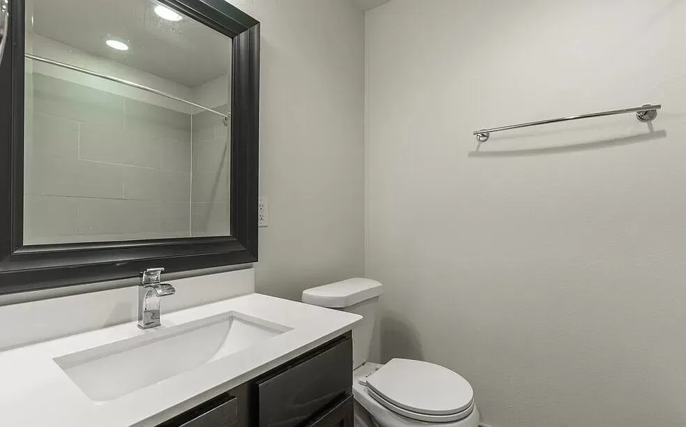 Bathroom with a white vanity, black-framed mirror, and a toilet beside a tiled shower