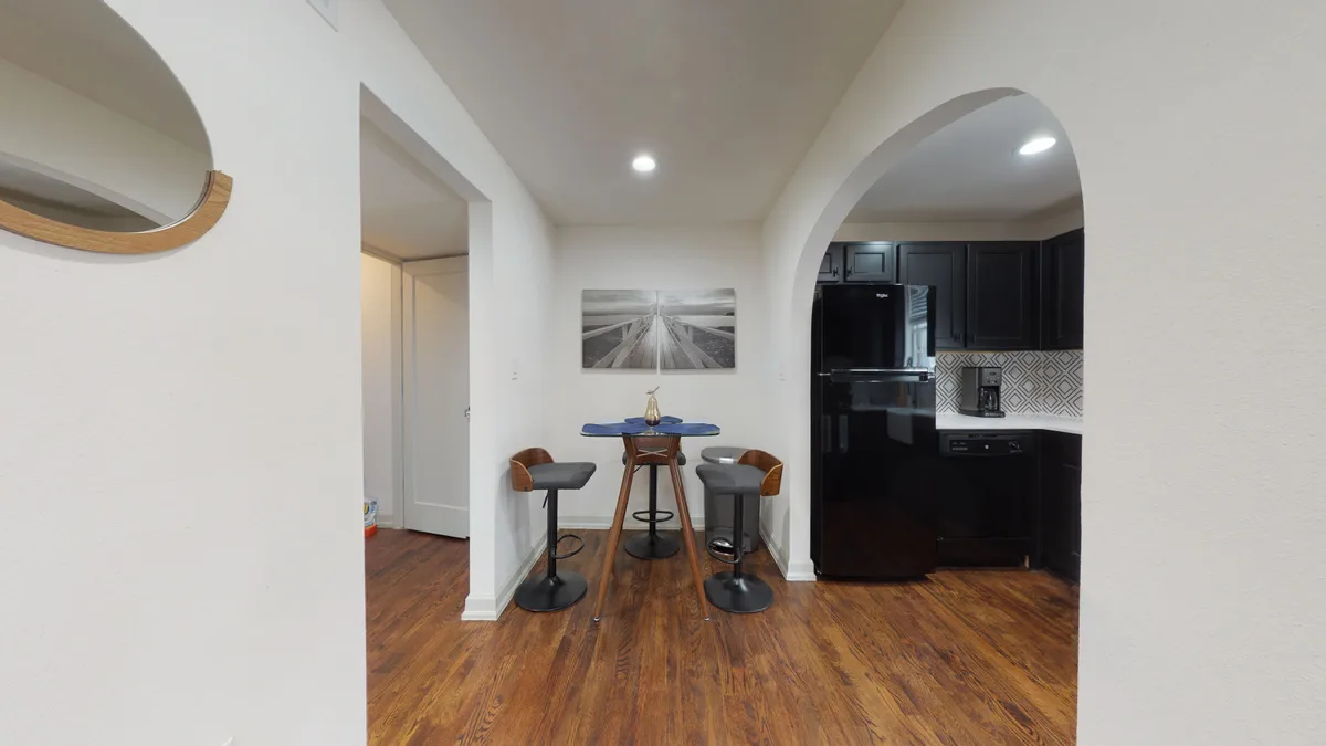 Dining nook with round bistro table and swivel stools beside an arched entry into the black kitchen