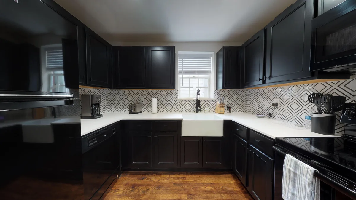 Kitchen with black shaker cabinets, white quartz counters, farmhouse sink and diamond-patterned backsplash