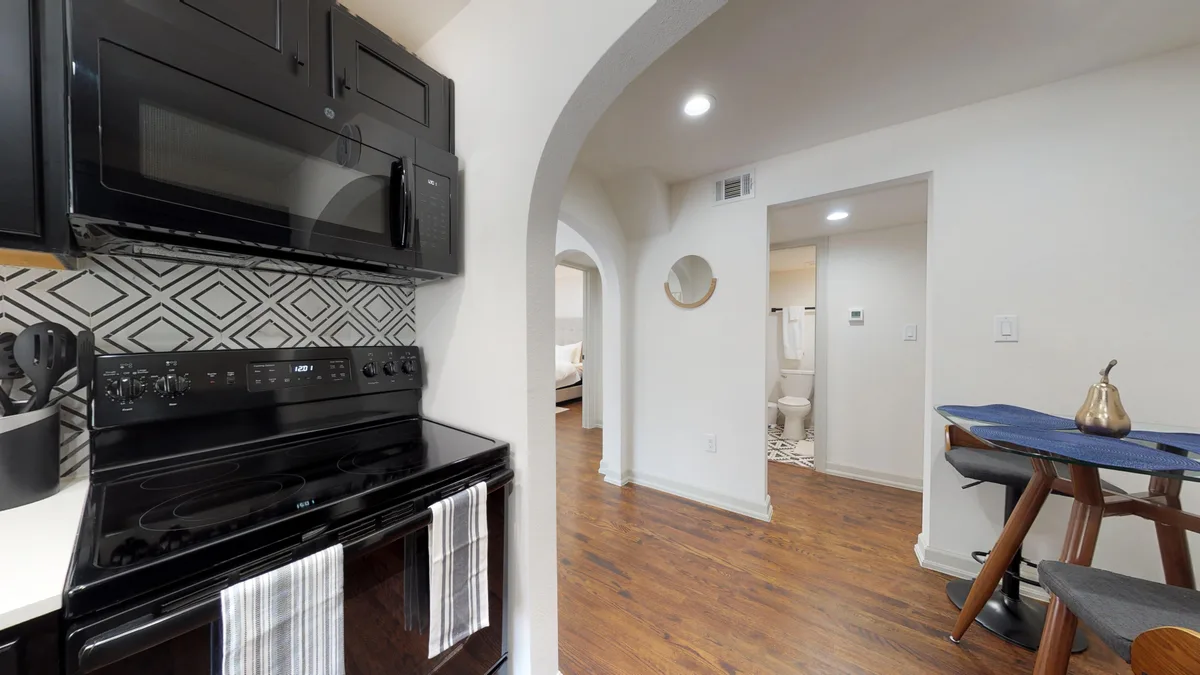 Black range and over-range microwave beside an arched hall leading to the bedroom and bathroom