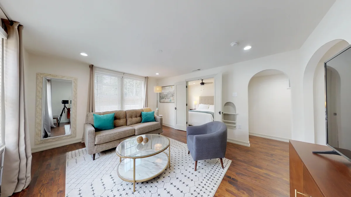 Living area opening through an arched doorway to the bedroom, with hardwood floors and a full-length floor mirror