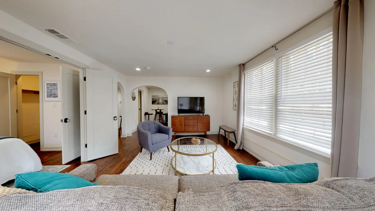 Open living and dining space with hardwood floors, arched openings and a wall of blinds-covered windows