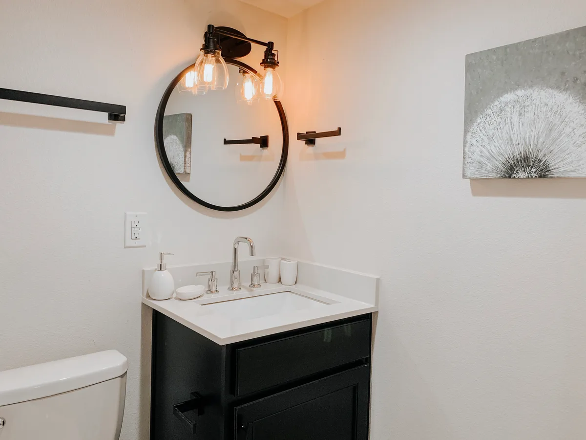 Bathroom vanity with black cabinetry, white quartz top, round mirror and an Edison-bulb sconce