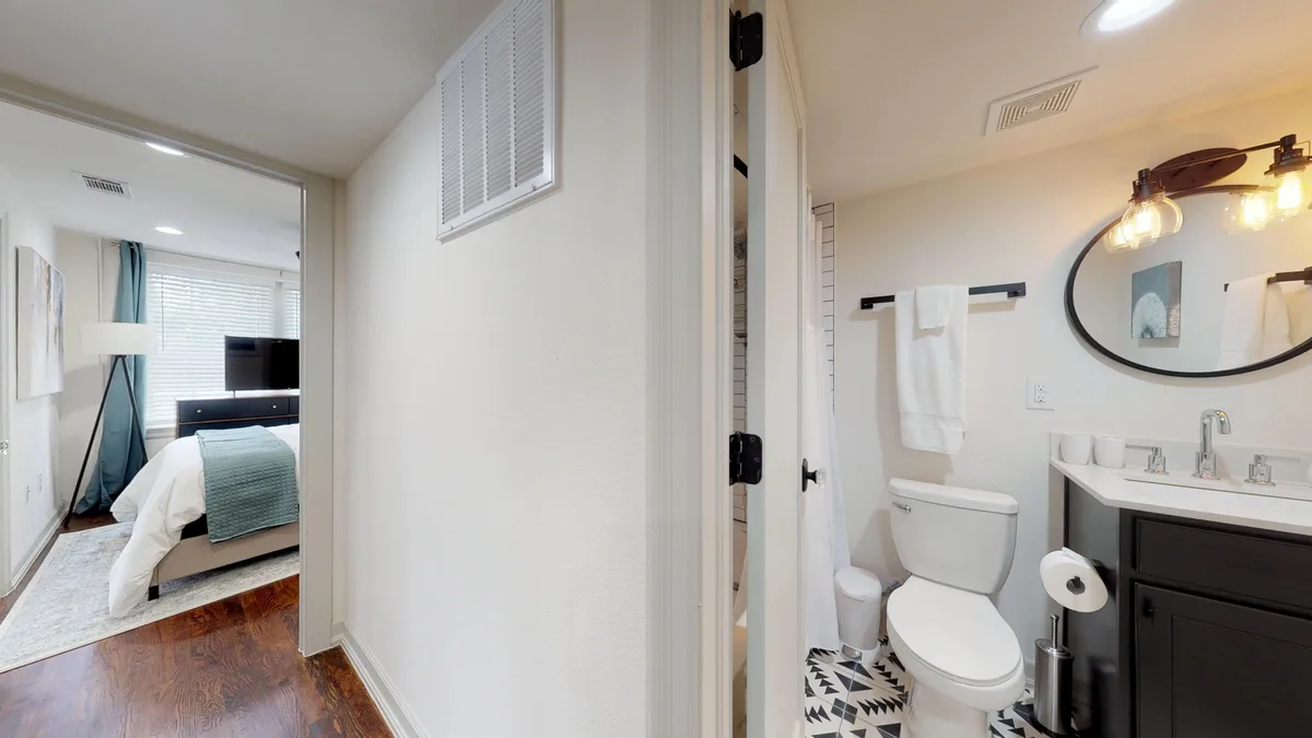 Bathroom with dark vanity, round mirror and patterned floor tile, opening toward the bedroom