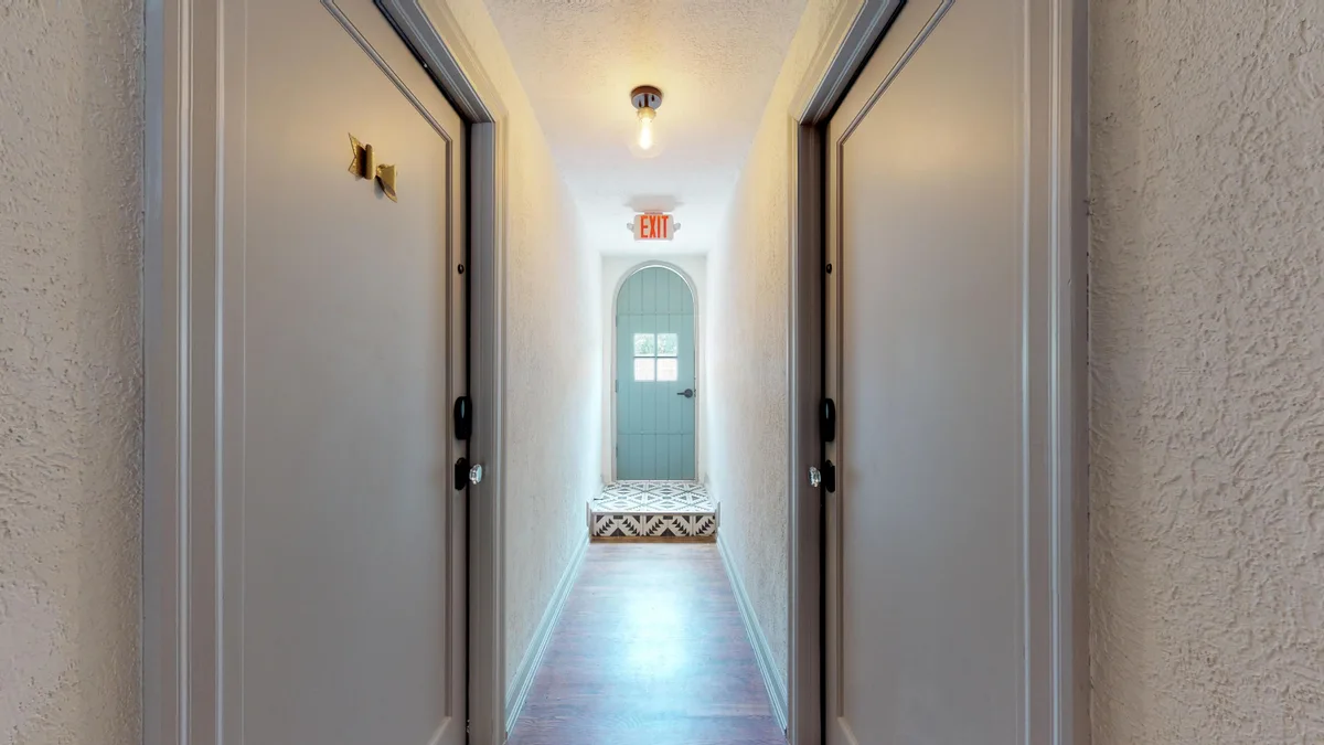 Resident corridor with hardwood floors and doors on both sides leading to an arched sage-green exit door