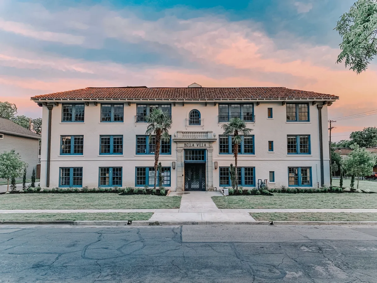 Symmetrical white stucco facade at sunset with clay-tile roof, palm trees and BELLA VILLA carved above the entry