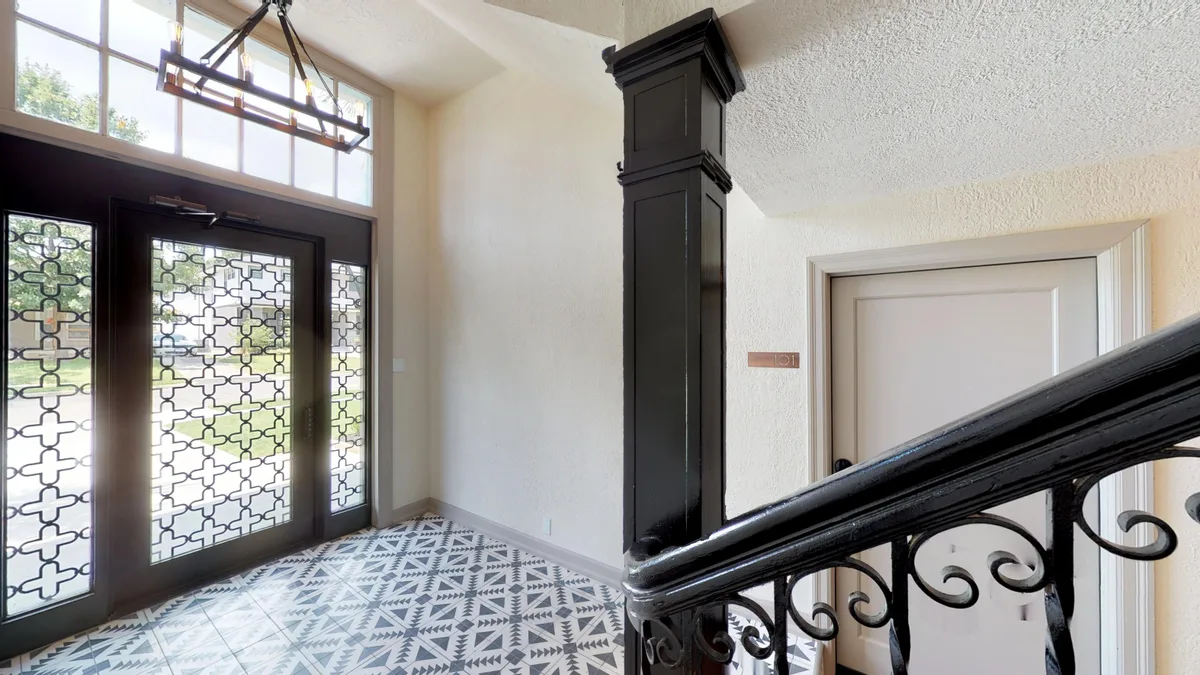Interior entry lobby with patterned black-and-white tile, decorative glass doors and a wrought-iron staircase
