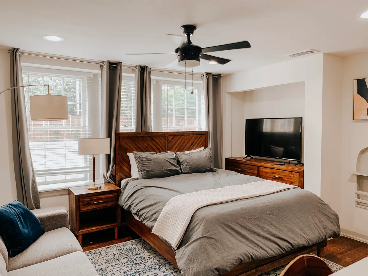 Studio bedroom with wood chevron headboard, gray linens, matching nightstands and a dresser-top TV