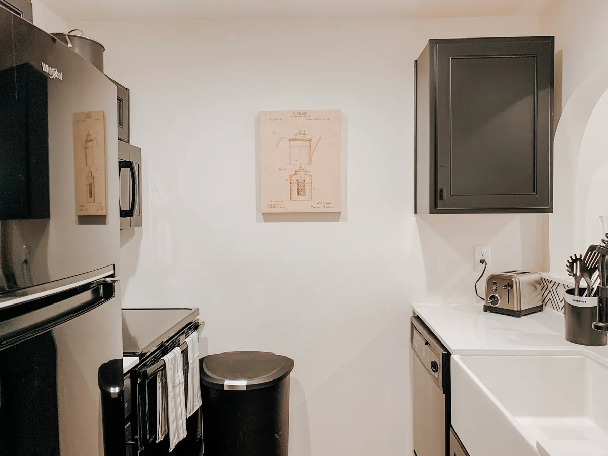 Galley kitchen with black refrigerator, range and cabinetry and a vintage coffee-pot patent print