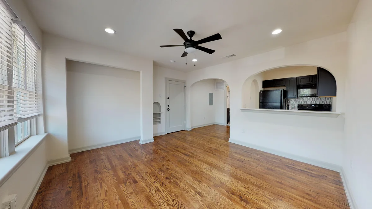 Empty open living area with arched kitchen pass-through, ceiling fan and a niche beside the front door