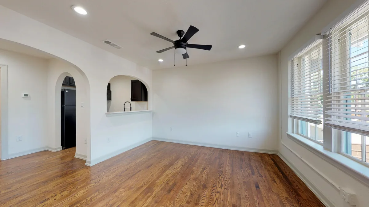 Vacant living room with an arched kitchen bar opening, black refrigerator and corner windows