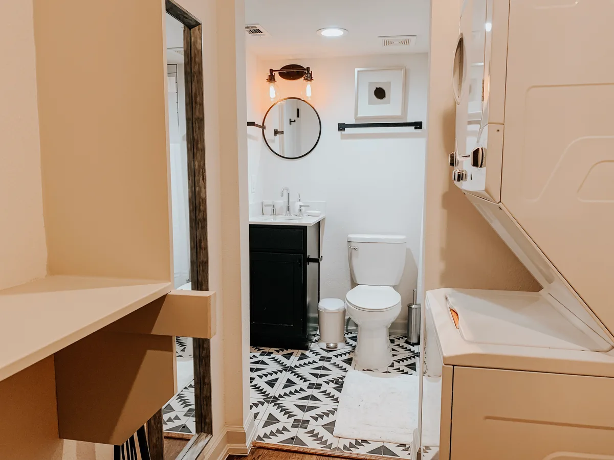 Bathroom with black vanity, round mirror and patterned tile floor, with a stacked washer-dryer alongside