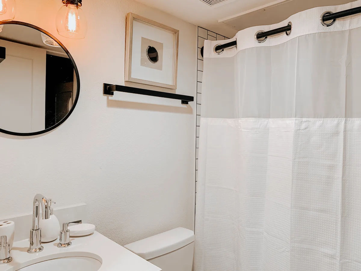 Bathroom vanity and round mirror beside a subway-tiled tub with a white waffle shower curtain