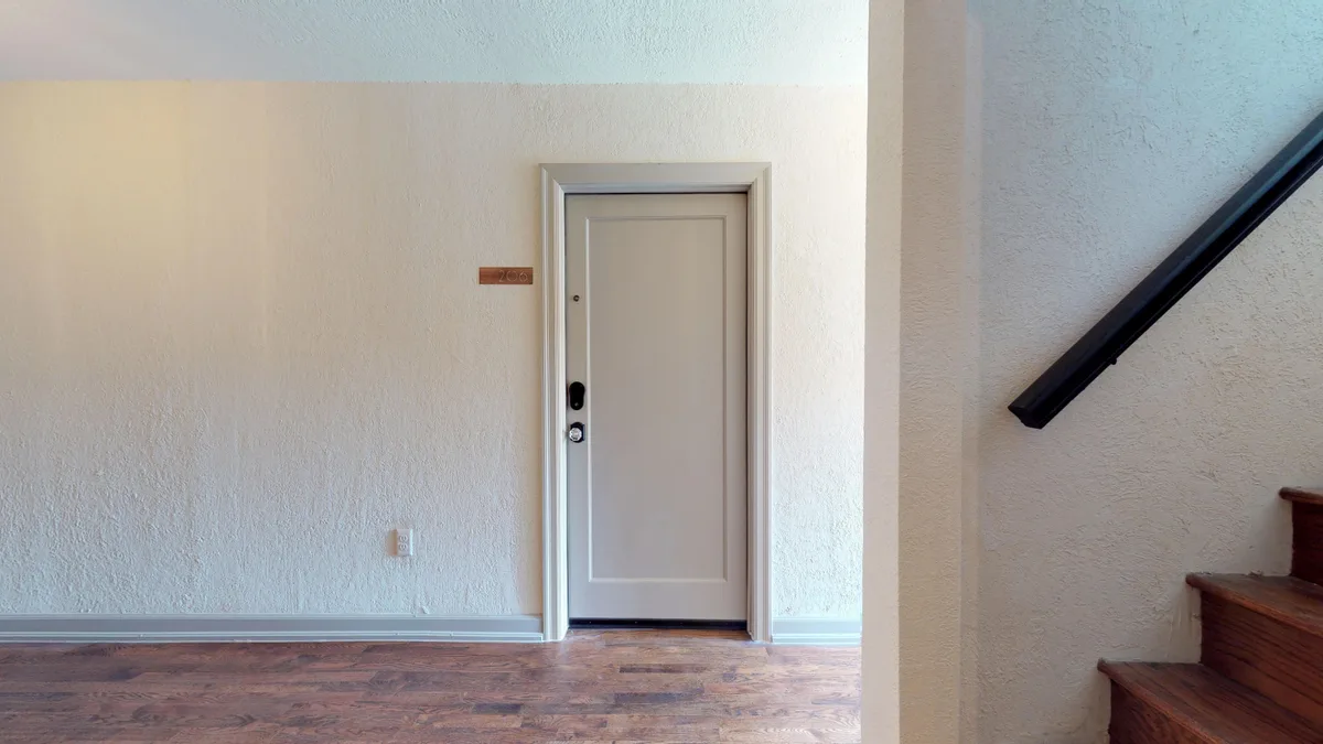 Interior stair landing with hardwood floors, black handrail and a unit door numbered 206
