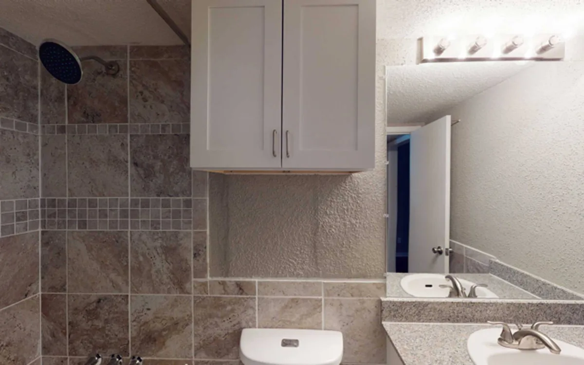 Bathroom with tiled tub-shower, rainfall showerhead, granite vanity, and over-toilet storage cabinet