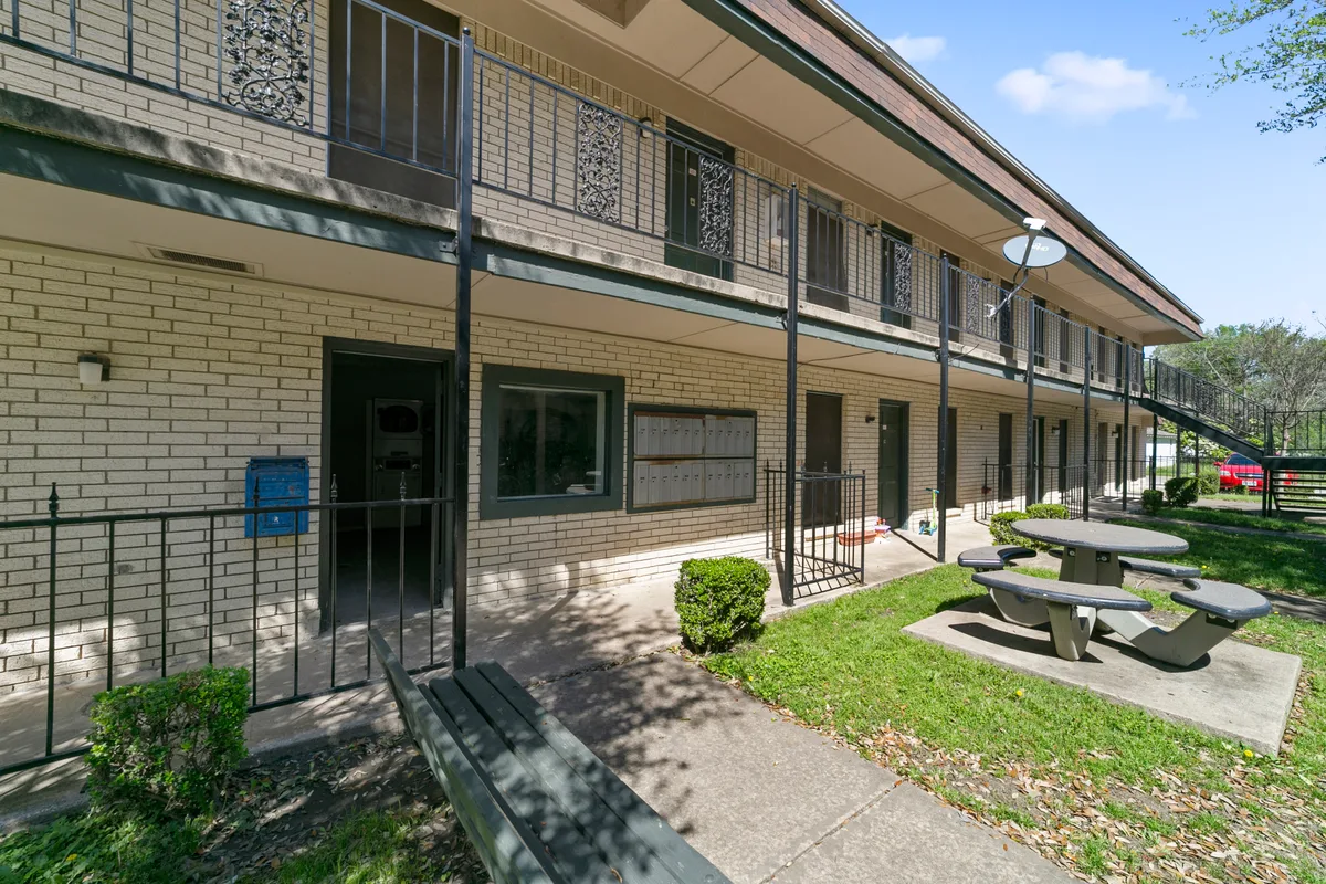 Ground-floor breezeway with cluster mailboxes, a picnic table, and shaded courtyard seating