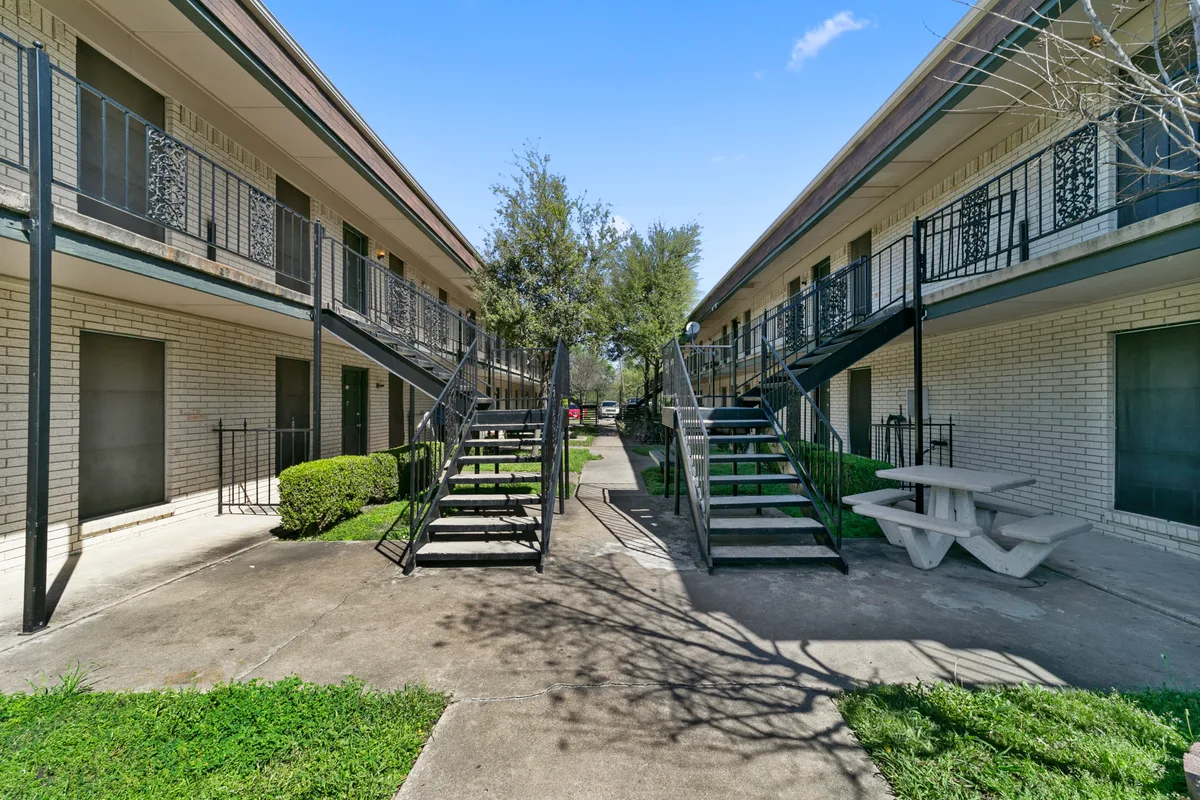 Interior courtyard framed by two-story buildings with wrought-iron staircases and a picnic table