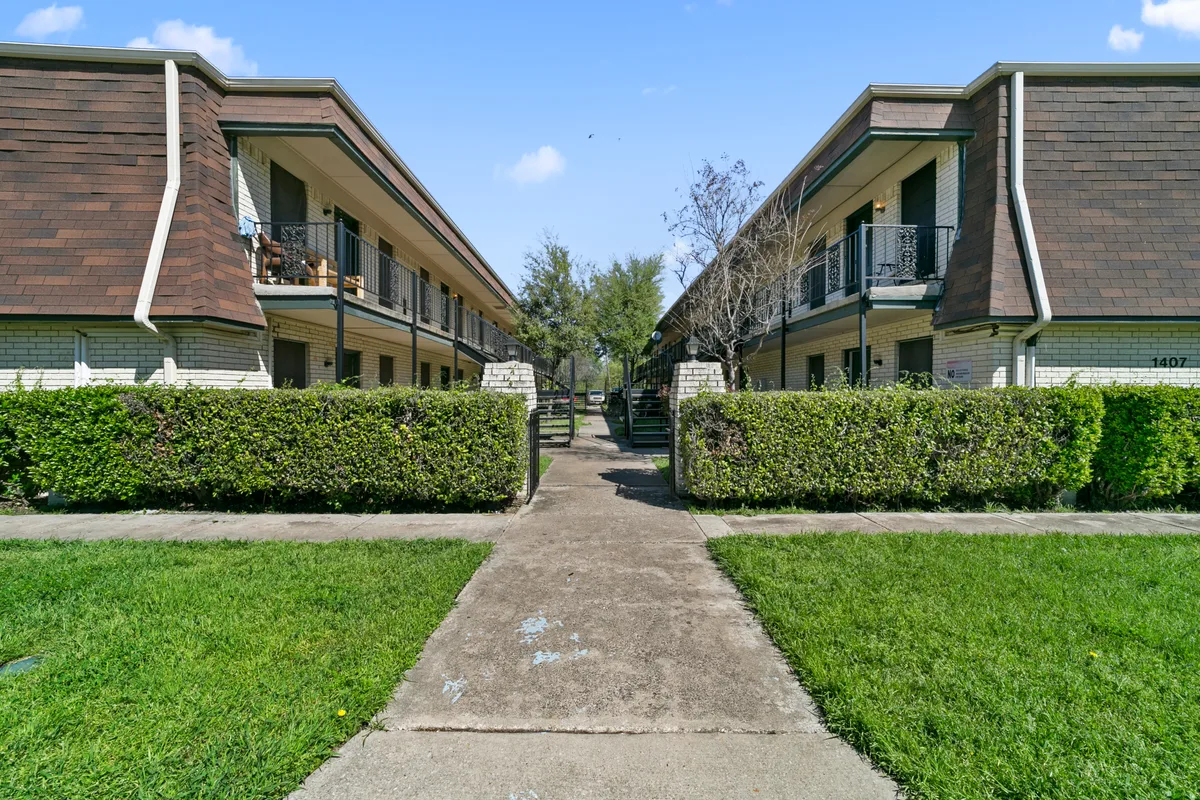 Landscaped front walkway between two-story buildings with mansard roofs and trimmed hedges