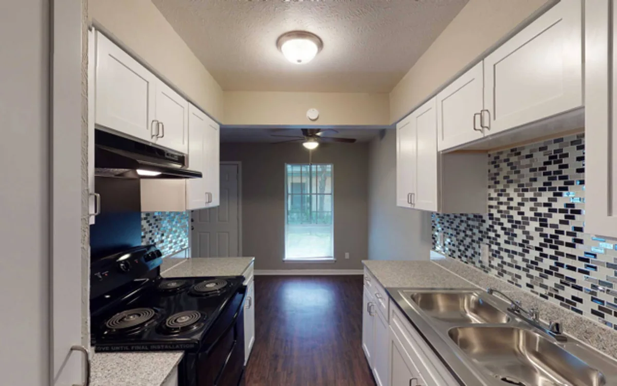 Galley kitchen with white cabinets, glass-tile backsplash, black appliances, and a sunny dining nook