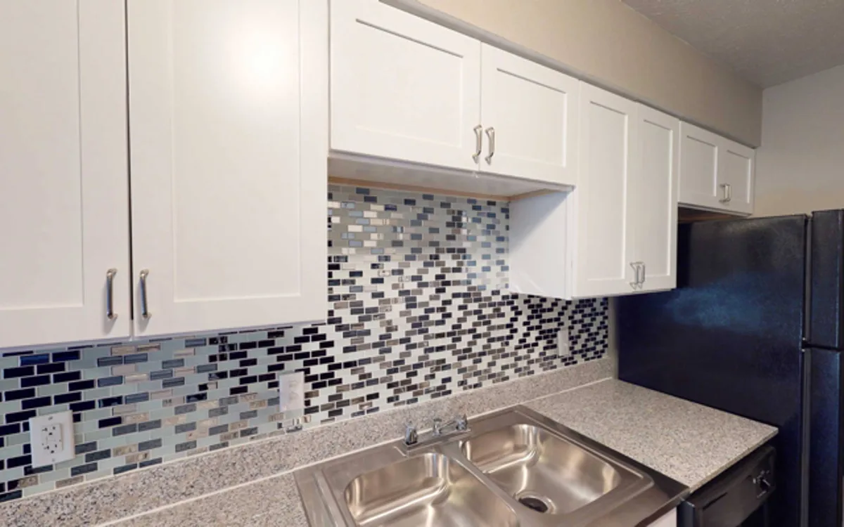Kitchen detail showing mosaic glass-tile backsplash, granite-look counters, and a stainless double sink