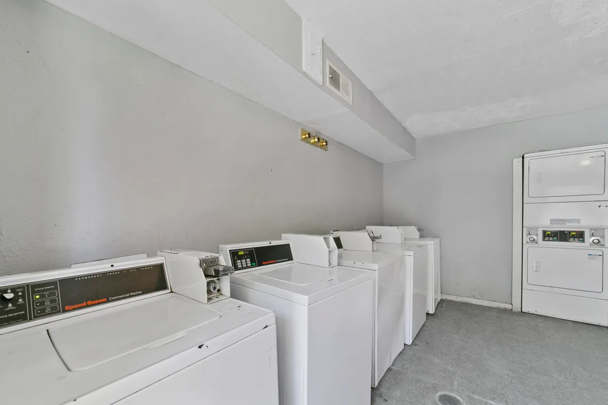 Shared laundry room with multiple top-load washers and stacked commercial dryers