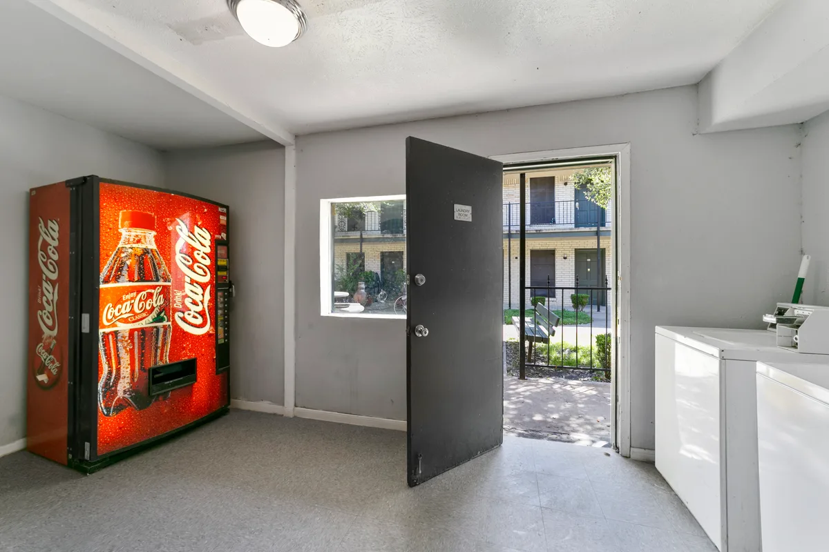 Laundry room with a soda vending machine and a door opening to the courtyard