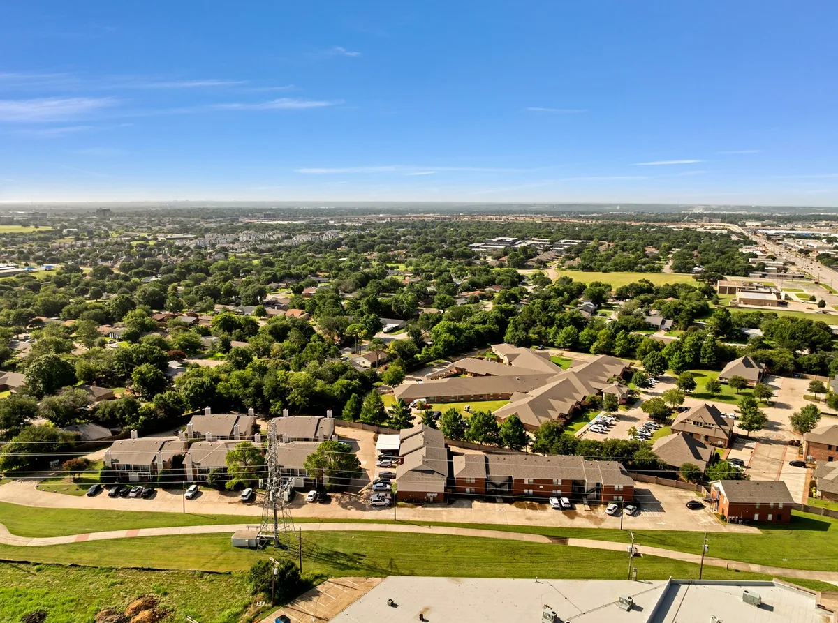 Aerial view of the Davis Square community's brown-roofed townhome buildings, tree-lined streets, and parking, with the Fort Worth skyline on the horizon