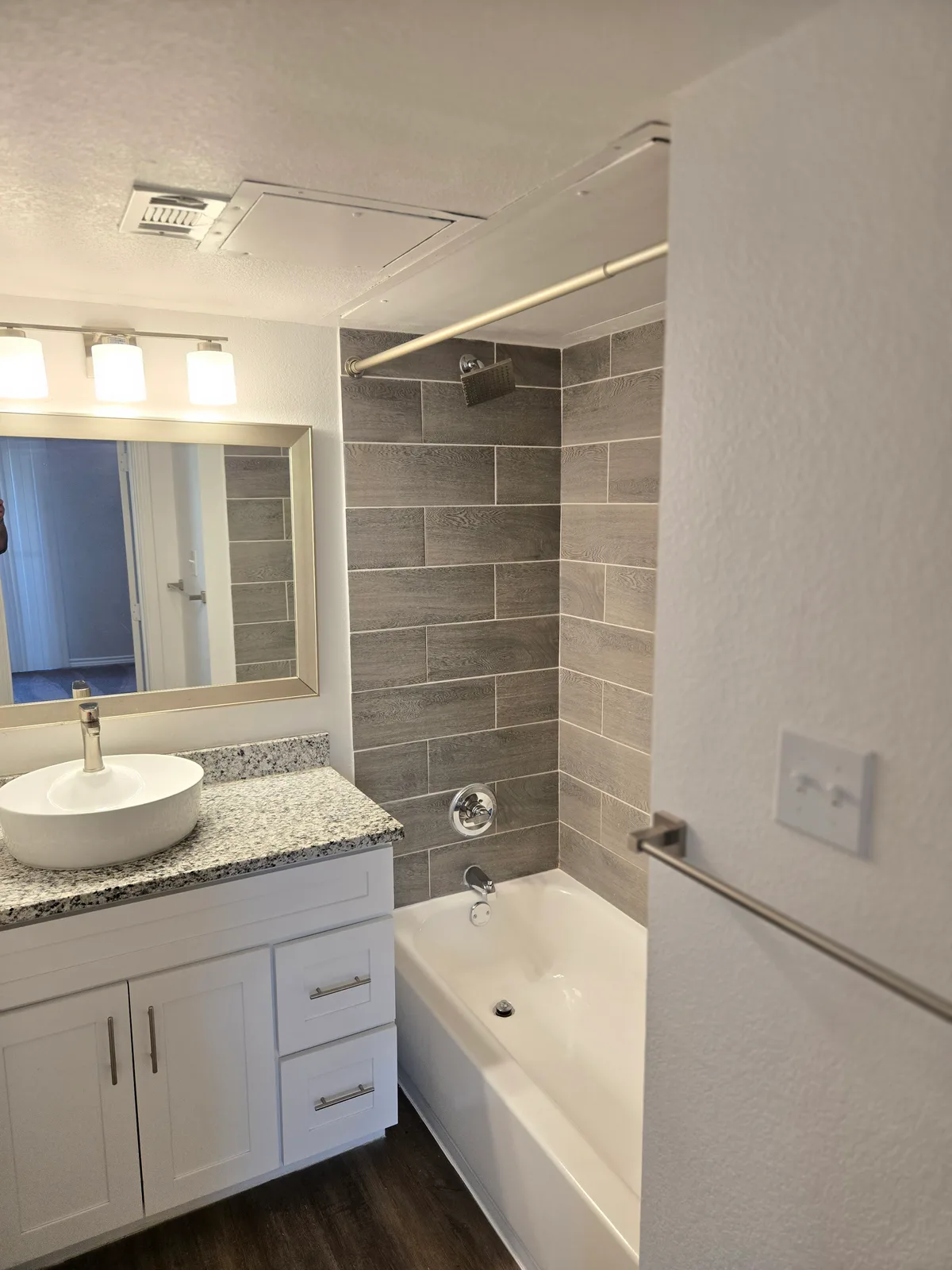 Bathroom with a gray wood-look tiled tub-and-shower surround, a granite-topped vanity with a vessel sink, and a framed mirror