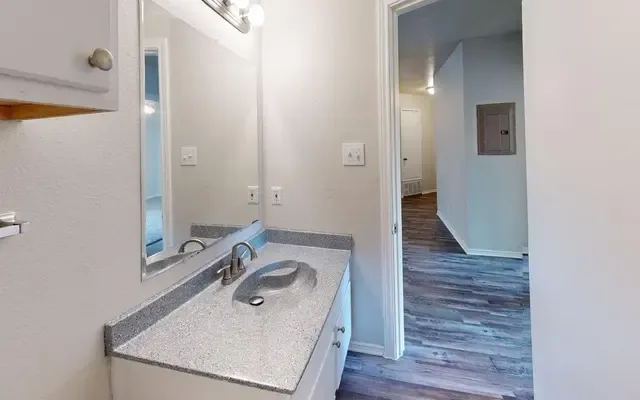 Bathroom vanity with a granite-look countertop, a framed mirror, and a medicine cabinet, opening to a wood-floored hallway