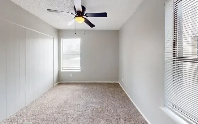 Carpeted bedroom with a dark-blade ceiling fan, a blinded window, and a wood-paneled accent wall