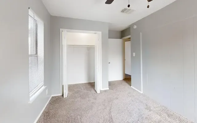 Carpeted bedroom with an open double closet, a ceiling fan, and a doorway to the hall
