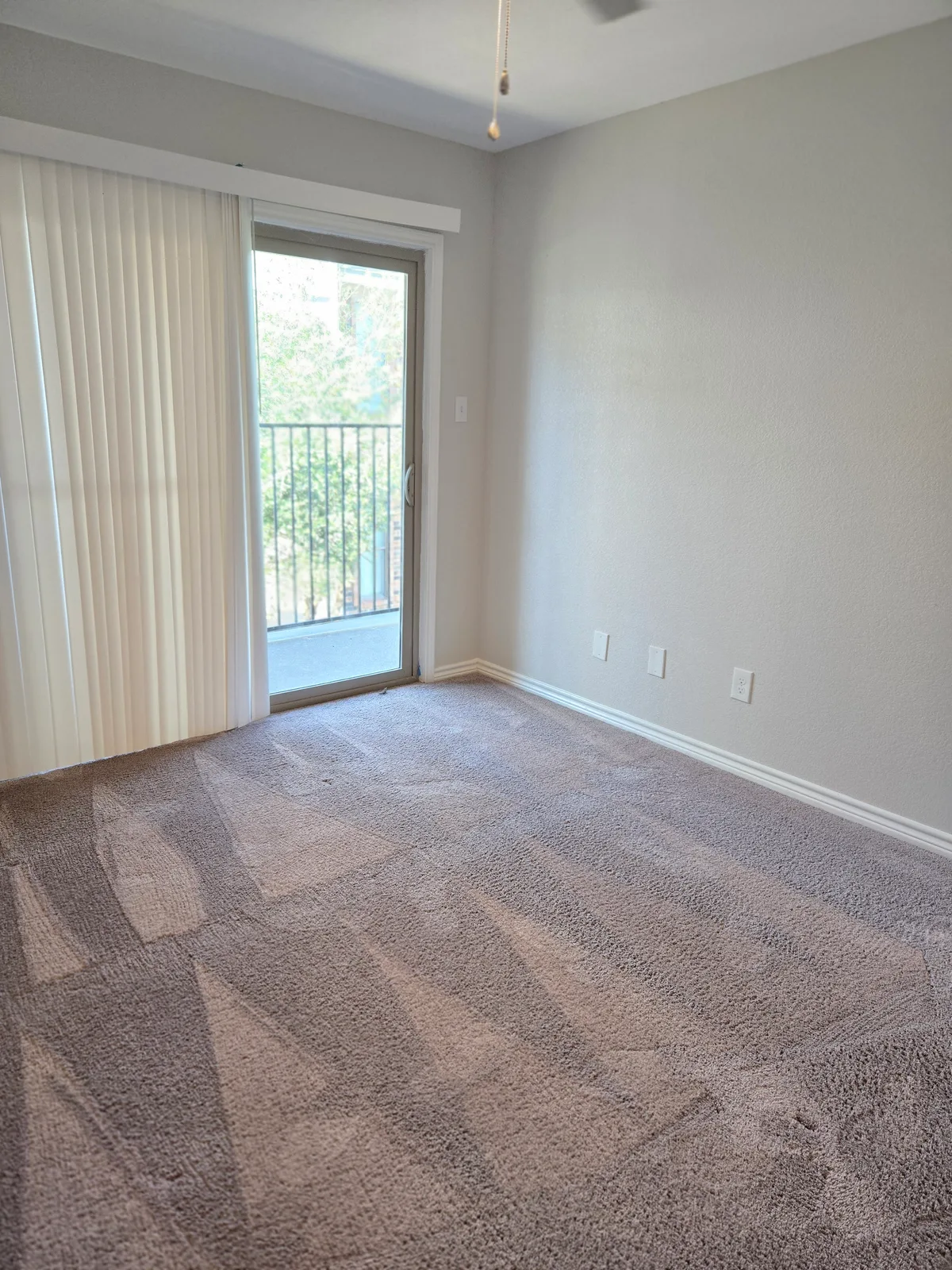 Carpeted bedroom with a sliding glass door opening to a private railed balcony