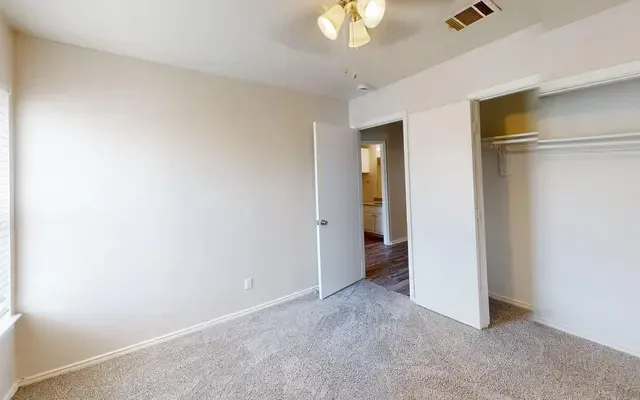 Empty carpeted bedroom with a ceiling fan and an open double-door closet with a hanging rod and shelf