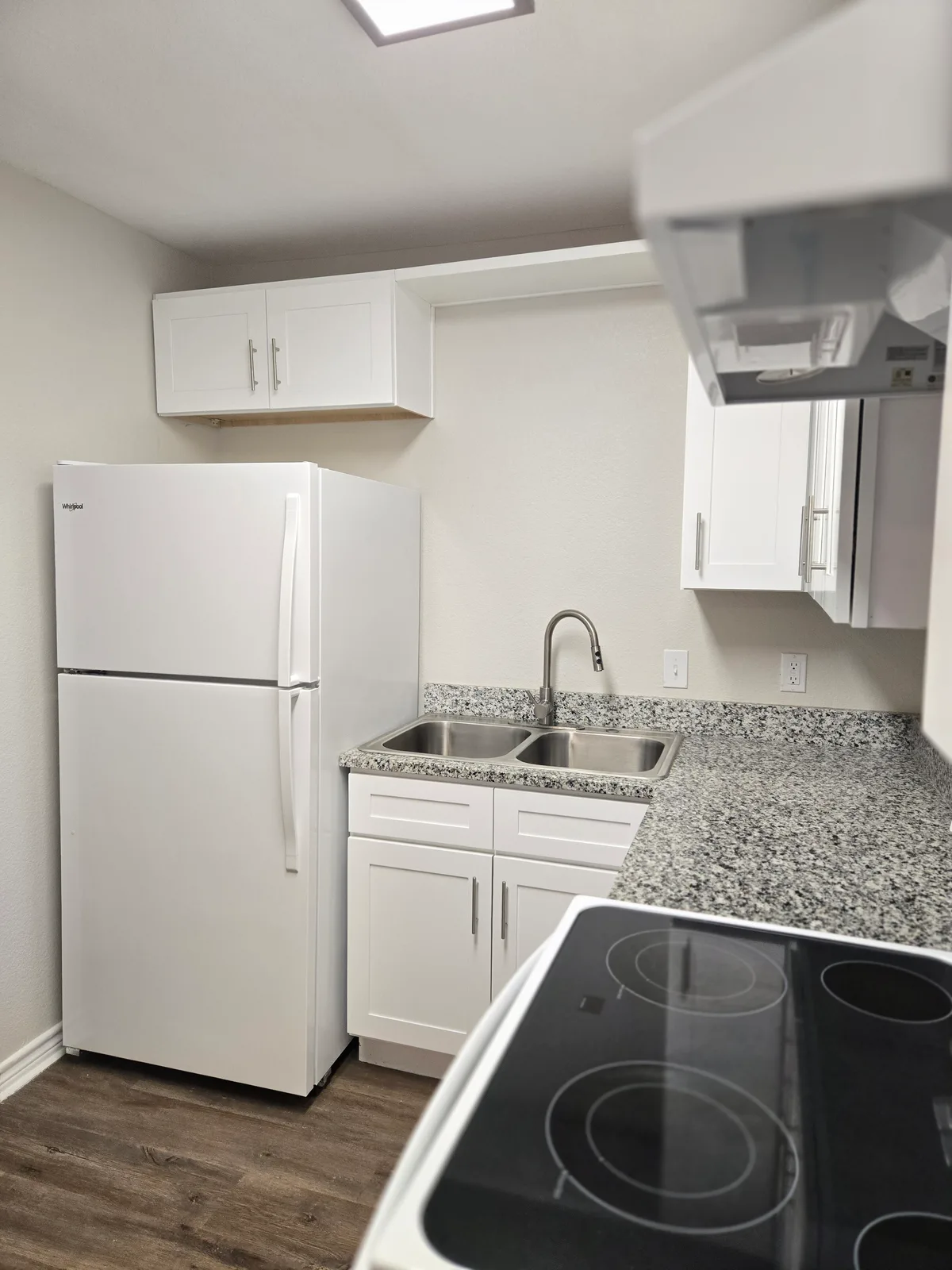 Kitchen corner with a white refrigerator, granite counters, a stainless double sink, and a glass-top electric range