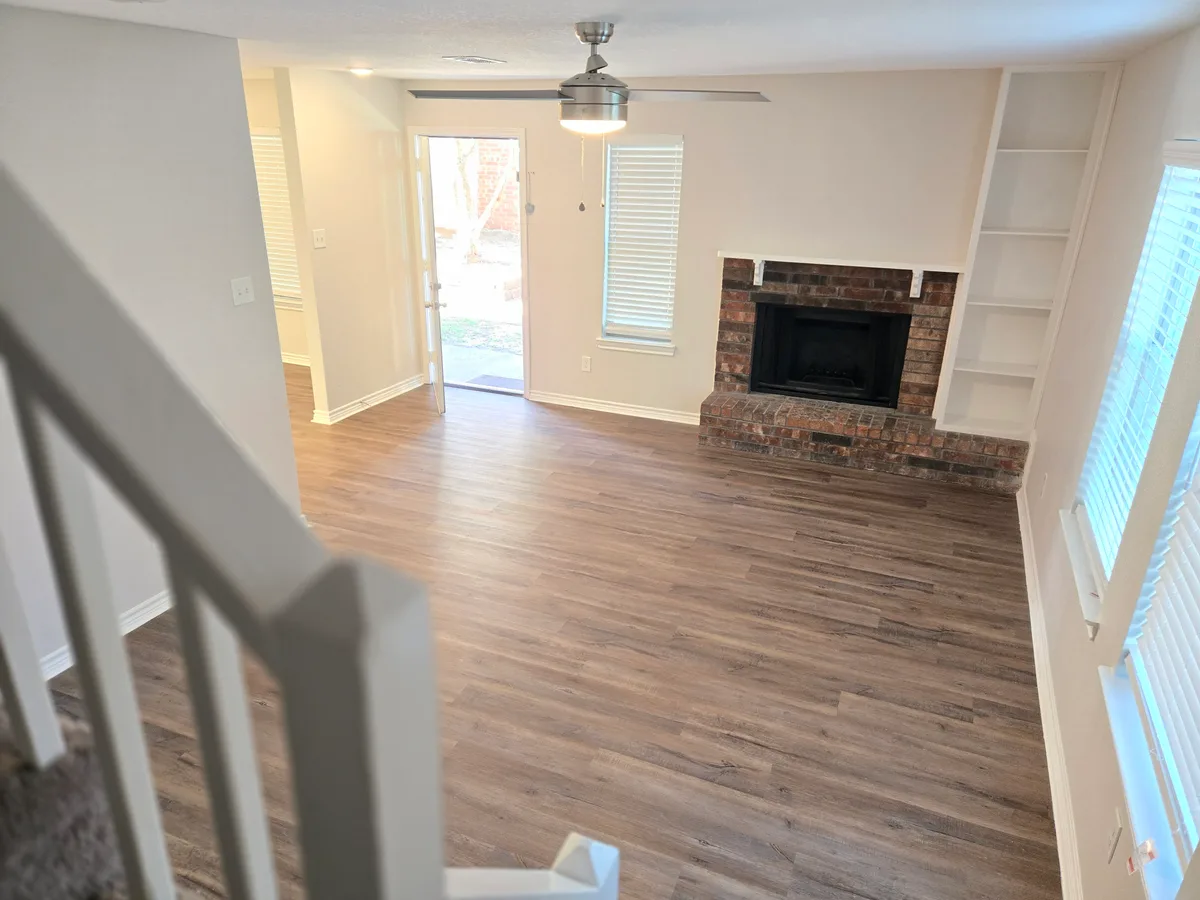 Open living room with a red-brick fireplace, white built-in bookshelves, wood-look floors, and an exterior door letting in daylight