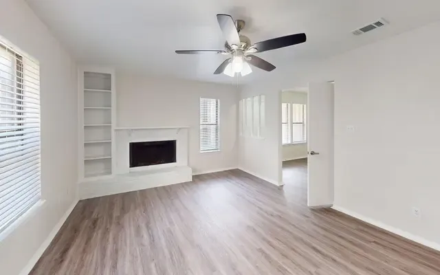 Living room with a white-surround fireplace, built-in white shelving, wood-look plank flooring, and a ceiling fan