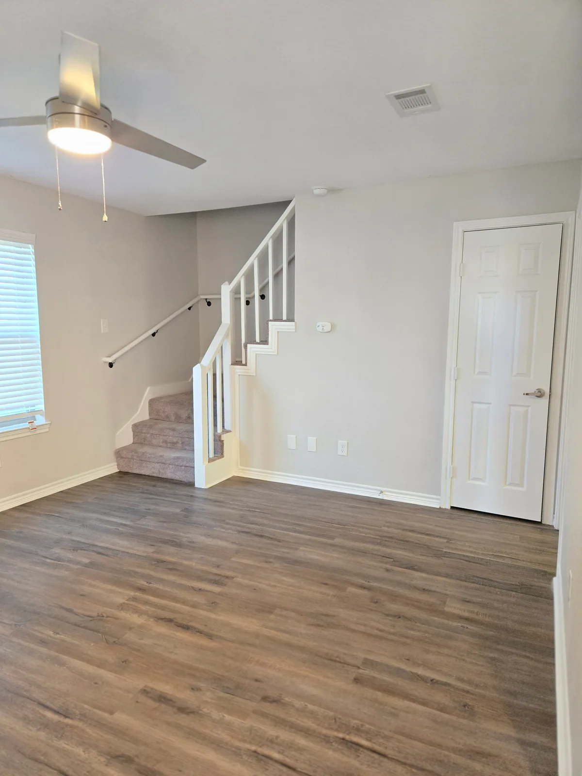 Living room opening to a carpeted staircase with a white railing, wood-look flooring, and a ceiling fan