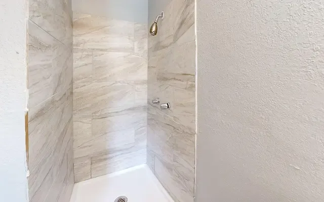 Walk-in shower stall with marble-look tile walls, a chrome shower head, and a white shower base